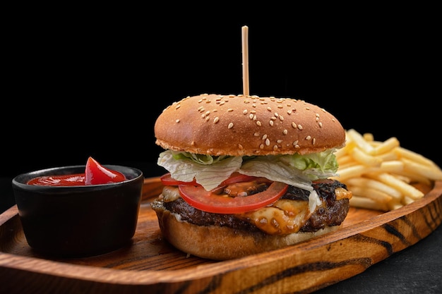 Hamburguesa con carne, tomates y queso, patatas fritas y salsa sobre un fondo negro