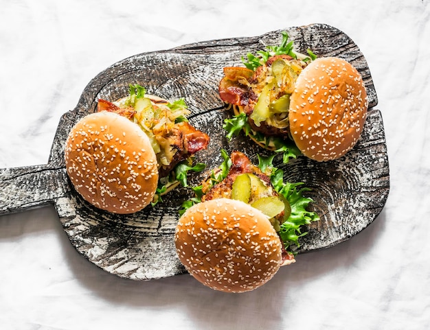 Hamburguesa casera clásica con chuleta de cerdo, tocino, pepinillos, cebollas fritas y mayonesa, salsa de mostaza en una tabla de cortar de madera