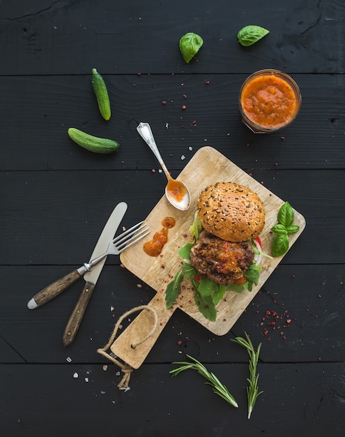 Foto hamburguesa casera fresca en una tabla oscura con salsa de tomate picante, sal marina y hierbas
