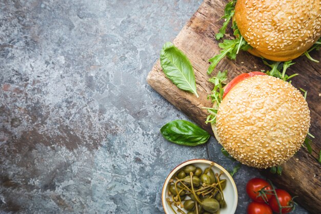 Hamburguesa casera fresca en tablero para servir con salsa picante y hierbas sobre fondo de piedra oscura. Vista superior con espacio de copia.