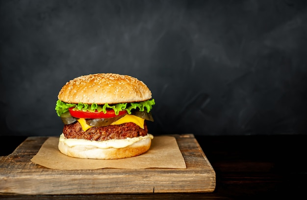 Hamburguesa casera con lechuga, tomate, queso y pepino en una tabla de cortar con espacio de copia para su texto