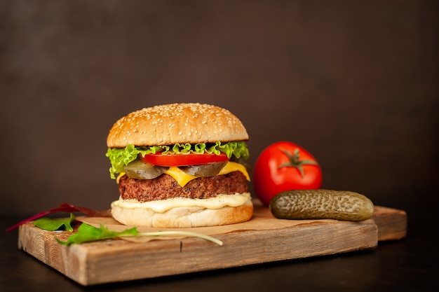 Hamburguesa casera con lechuga, tomate, queso y pepino en una tabla para cortar