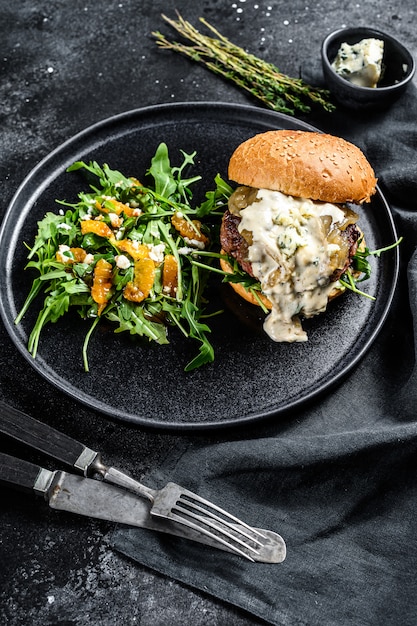 Hamburguesa casera con queso azul, tocino, carne marmolada y mermelada de cebolla, una guarnición de ensalada con rúcula y naranjas. .