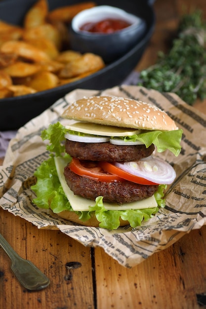 Foto hamburguesa casera con rodajas de patata sobre una mesa de madera, rústica, enfoque selectivo