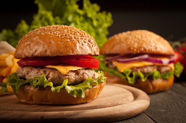 Hamburguesa casera con ternera, cebolla, tomate, lechuga y queso. Hamburguesa fresca de cerca en la mesa rústica de madera con papas fritas, cerveza y patatas fritas. Hamburguesa con queso.