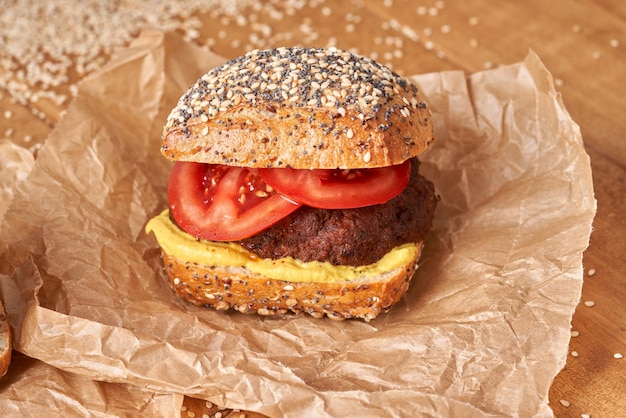 Hamburguesa casera con tomate y mostaza en la mesa de madera.