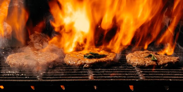 Foto hamburguesa de chuleta a la parrilla con filete de res crudo en llamas en un lugar de receta de menú de banner de parrilla de barbacoa para vista superior de texto