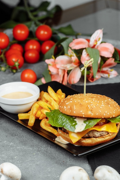 Hamburguesa con chuleta, queso y tomates. Con patatas fritas y salsa de hamburguesa.