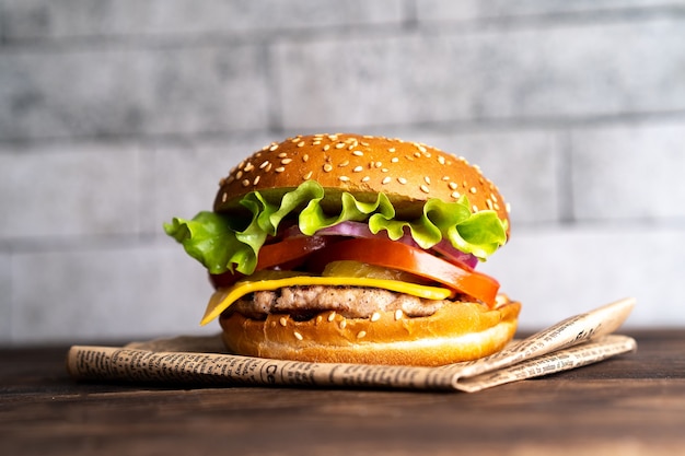 Hamburguesa con chuleta, tomate y queso sobre una mesa de madera oscura y papel.