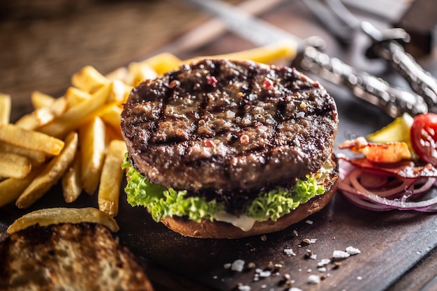 Foto hamburguesa clásica de carne con ensalada, cebolla y papas fritas.