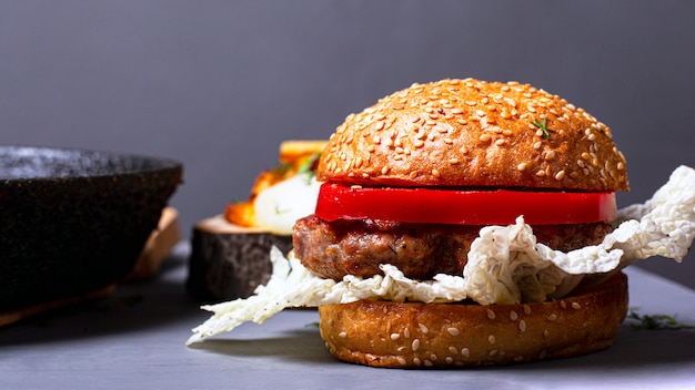 Hamburguesa clásica casera con col china, chuleta jugosa y pimiento dulce sobre un fondo gris.