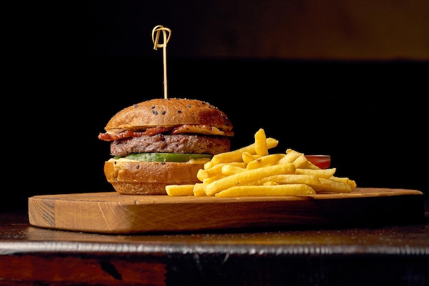 Hamburguesa de comida rápida americana con patatas fritas y salsa. Fondo de madera oscura. Enfoque selectivo.