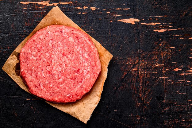 Foto hamburguesa cruda sobre papel sobre un fondo oscuro rústico