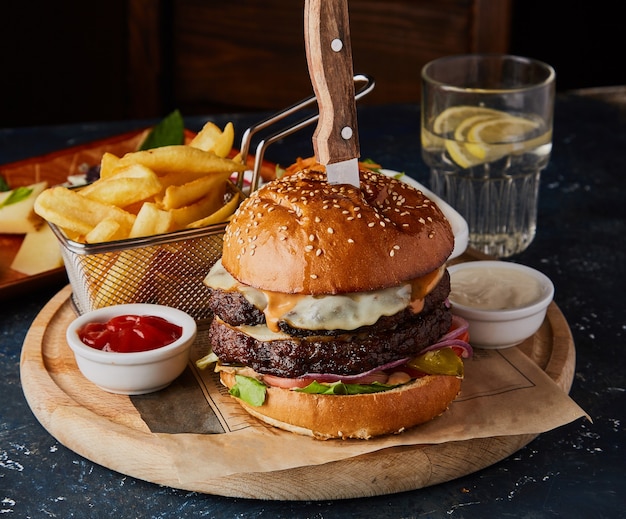 Hamburguesa doble de ternera con huevo, patatas fritas y salsas en la mesa.