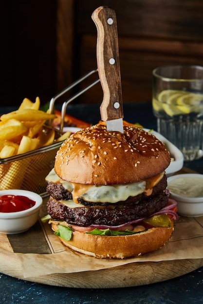 Hamburguesa doble de ternera con huevo, patatas fritas y salsas en la mesa.