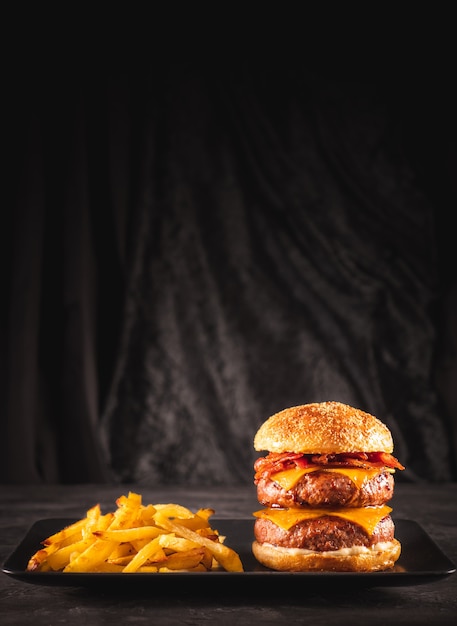 Hamburguesa doble de ternera y tocino con queso cheddar y patatas fritas sobre una mesa negra