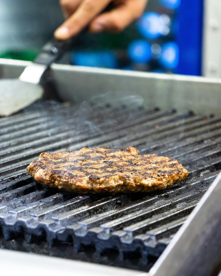 una hamburguesa está en una parrilla con una persona cocinando en ella