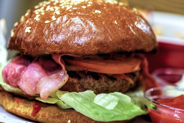 Hamburguesa fresca casera con tocino en un plato de madera closeup, salsa de tomate y ensalada