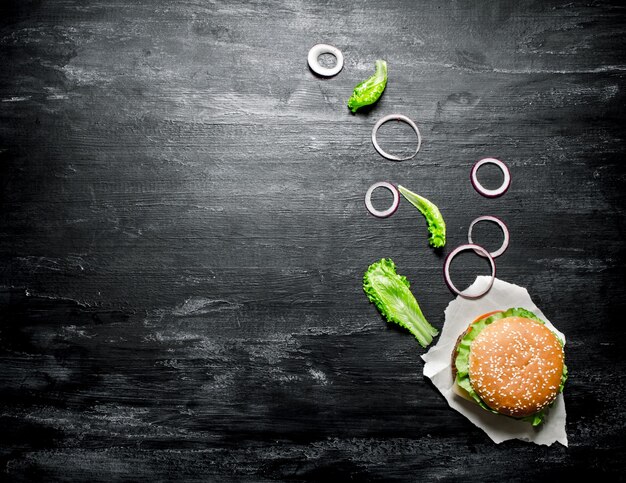 Hamburguesa fresca con cebollas y hierbas. En una pizarra negra. Vista superior.