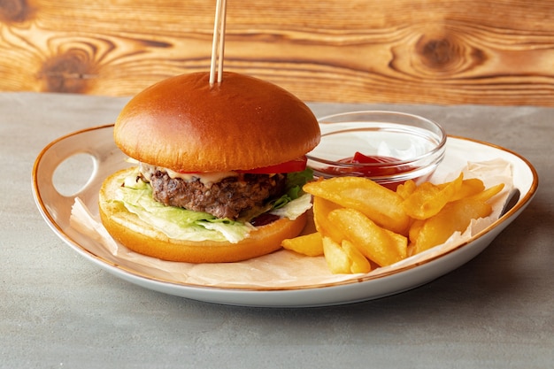 Hamburguesa fresca y gajos de patata sobre fondo de madera gris