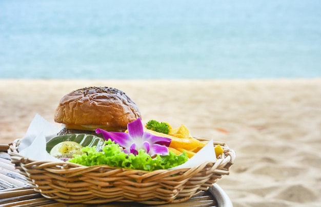 Foto hamburguesa fresca con papas fritas en una mesa de madera con fondo de playa