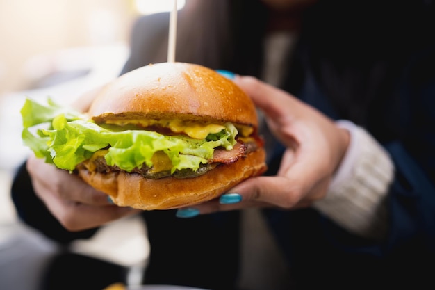 Hamburguesa gourmet de primer plano retenida por una hembra recortada irreconocible. Fondo borroso.