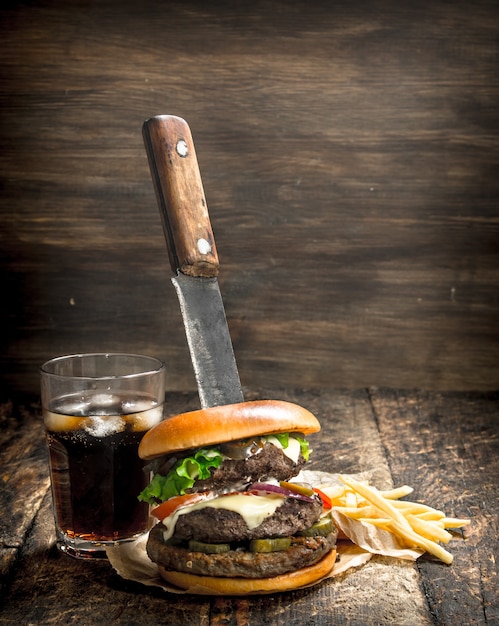 Hamburguesa grande con cola y papas fritas. Sobre una mesa de madera.