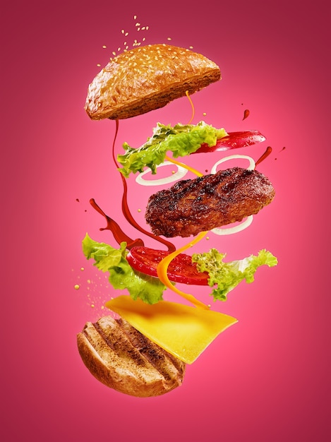 La hamburguesa con ingredientes voladores sobre fondo rosa. Concepto de publicidad