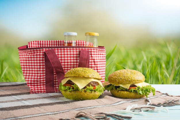 Hamburguesa de jugo a cuadros y una bolsa de picnic bajo el cálido sol en los florecientes jardines de primavera Concepto de picnic de verano y descanso