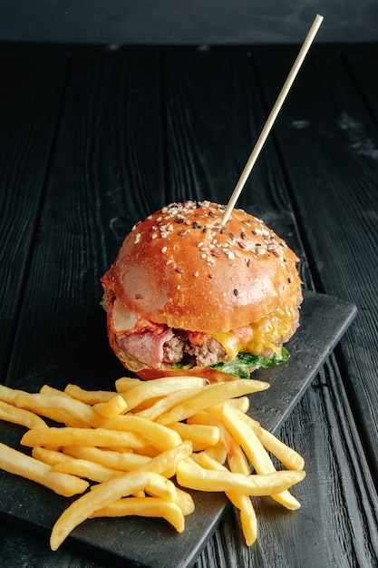 Hamburguesa jugosa casera en tablero de madera oscura.