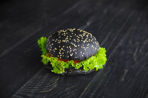 Hamburguesa negra espolvoreada con semillas de sésamo sobre madera con textura negra