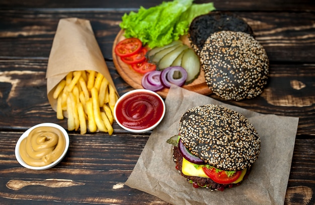 hamburguesa negra con lechuga, tomate y papas fritas. Fondo de madera