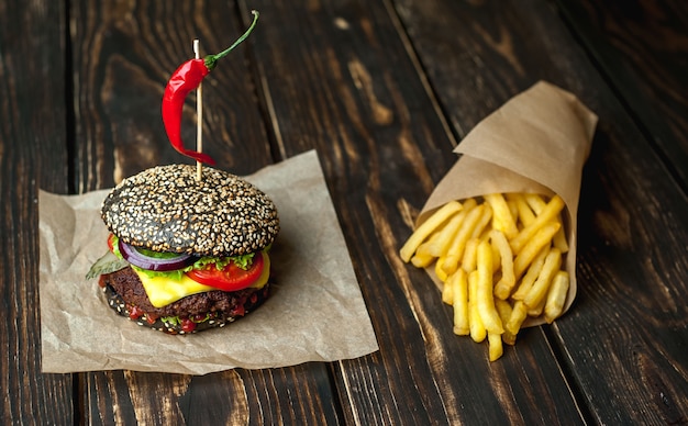 hamburguesa negra con lechuga, tomate y papas fritas. Fondo de madera