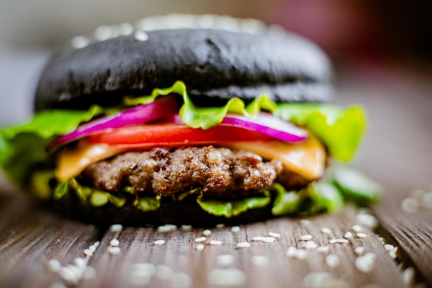 Hamburguesa negra de primer plano con carne artificial y vegetación fresca en la mesa de madera Enfoque selectivo