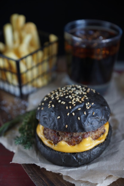 Hamburguesa negra sobre papel artesanal en tabla de cortar con papas fritas y coca cola