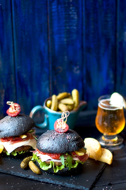 Hamburguesa negra con ternera, ensalada y papas fritas. Cerveza fresca en un vaso. Tendencias de la comida callejera. Una cena calórica. Copia espacio