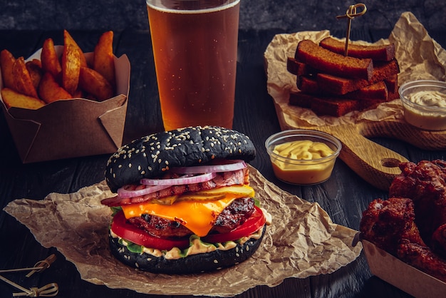 Hamburguesa negra de ternera con queso derretido y tocino, alitas de pollo frito, papas fritas