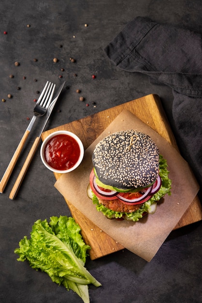 Hamburguesa negra vegetariana saludable con salsa de tomate y verduras hormiga sobre una tabla de cortar sobre un fondo oscuro. Vista superior y espacio de copia