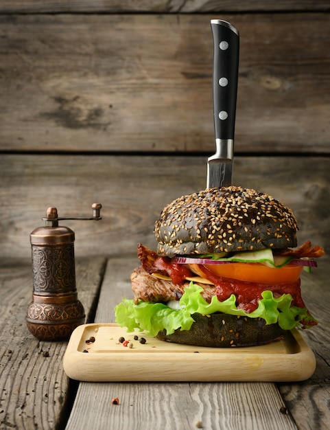 Hamburguesa con pan negro, carne y verduras en una mesa de madera, comida rápida