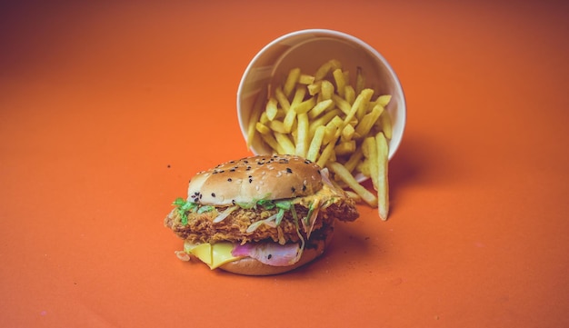 Hamburguesa y papas fritas aisladas en un fondo naranja Hamburguesa grasienta y papas fritas de un restaurante de comida rápida aislado en un espacio de copia de fondo naranja