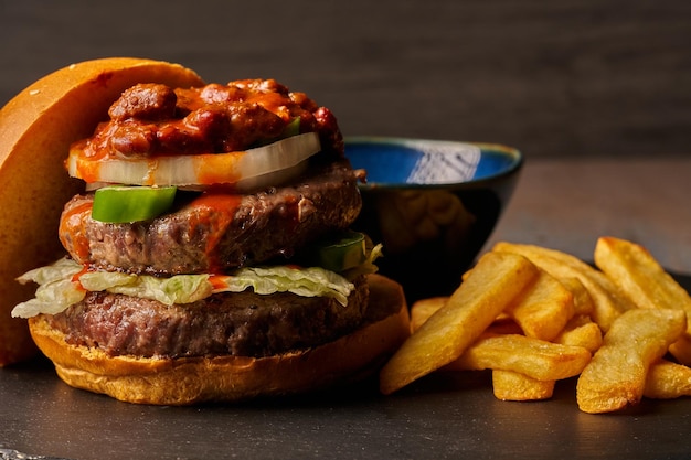 Hamburguesa con papas fritas cebolla chili con carne y jalapeños salsa barbacoa comida de estilo oscuro