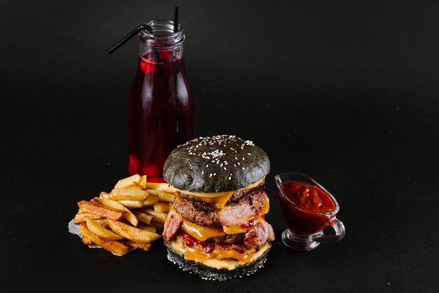 Una hamburguesa con papas fritas, salsa de tomate y un vaso de jugo en el fondo negro