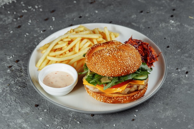 Hamburguesa de pavo en pan con queso, lechuga, tomate y pepino fresco. Hamburguesa con chuleta de carne de pavo sobre un fondo gris con salsa de papas fritas y ensalada.