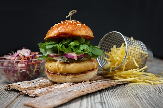 Hamburguesa de pescado en los platos de madera con queso, pepino, cebolla, ensalada verde y roja y papas fritas