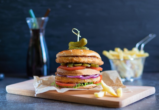 Hamburguesa de pollo con papas fritas y una botella de cocacola sobre un fondo oscuro