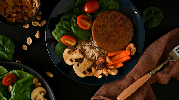 Hamburguesa de proteína de soja sobre arroz integral con espinacas, tomate, zanahoria campeona y nueces en un plato