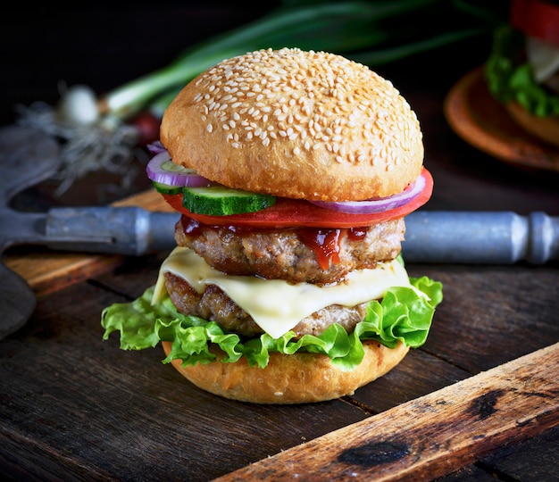 Hamburguesa con queso en un bollo con semillas de sésamo, en el medio de verduras frescas y chuletas de carne