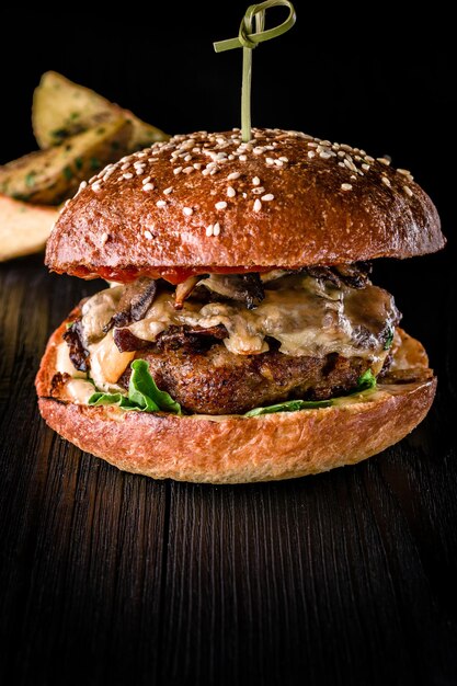 Hamburguesa de queso con carne a la parrilla, queso, tomate y patatas sobre superficie de madera oscura. Plantilla de comida rápida. Foto real. Ideal para publicidad. De cerca. Hamburguesa de bodegón