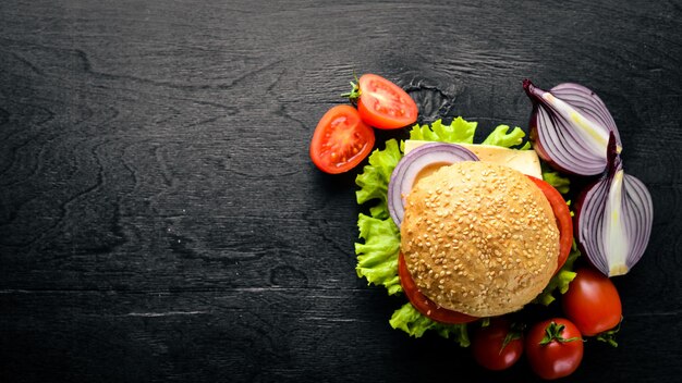 Hamburguesa con queso, carne, tomates, cebollas y hierbas Sobre fondo de madera Vista superior Espacio libre