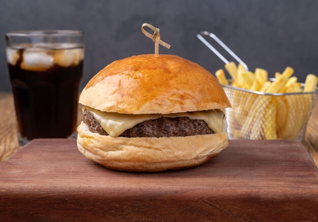 Hamburguesa de queso sobre tabla de madera con papas fritas y soda